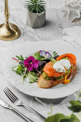 Bruschetta with Poached egg and fresh salmon , vegetarian salad with greens at the white plate on light marble background. Healthy sea food, hard light, restaurant decor