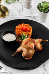 Roasted or fried quail with herbs and rise at black stone plate on light marble background. Healthy sea food, hard light, restaurant decor, close up