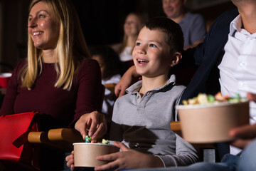 Family with son watching movie and eating popcorn in cinema hall