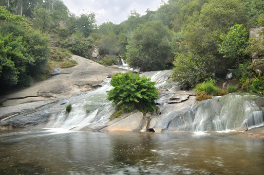 Cascata de um rio com po&ccedil;o de &aacute;gua no fim, tufos de vegeta&ccedil;&atilde;o e arbustos