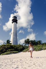Beautiful young blonde woman walking towards the Beach Florida Lighthouse. Cape Florida Lighthouse,...