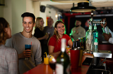 Young people with cocktails in hands chatting near the bar in nightclub. High quality photo - obrazy, fototapety, plakaty