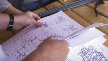 Naklejka premium Close up for hands of workers at a factory looking through technical drawings. Blueprints with sketches of projects, engineering concept.