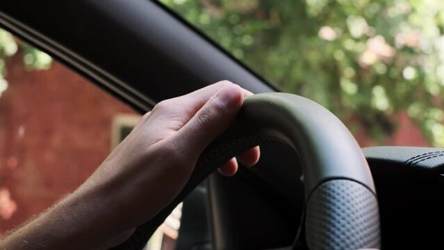 Handheld close up view of man hand turning steering wheel in car driving through city. unrecognizable man turns steering wheel in car and drives around town.