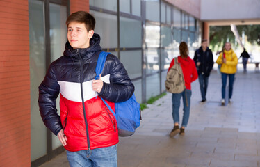 Obraz premium Portrait of teen boy with backpack walking to college campus on spring day..