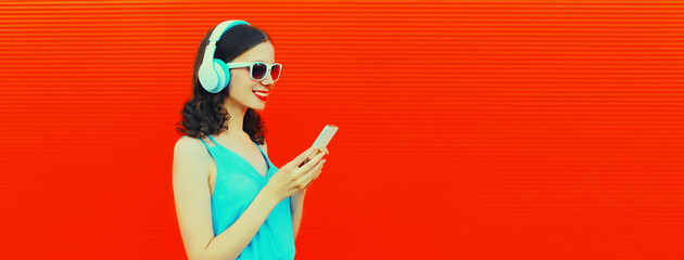 Portrait of happy smiling young woman in headphones listening to music with smartphone on red background, blank copy space for advertising text
