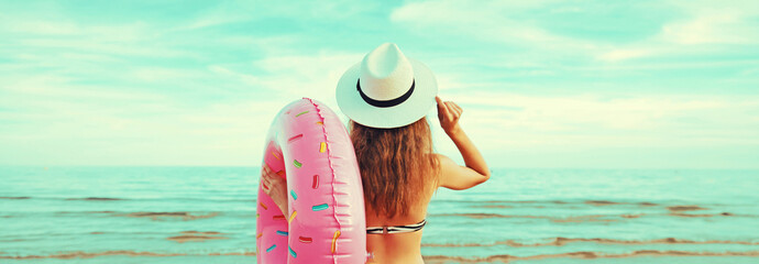 Portrait of happy smiling young woman with inflatable ring wearing straw hat on beach on sea background