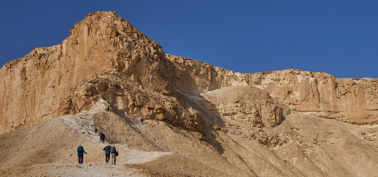 A group of hikers on a footpath to the top of mount Hod Akev, Negev desert, Israel. Popular hiking trail crossing Zin valley near Sde Boker settlement. Sunrise in the Negev desert. Vacation in Israel.