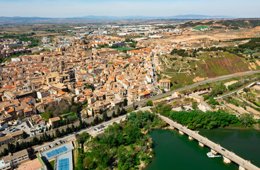 Fototapeta na wymiar Picturesque aerial view of historic center of Tudela with brownish tiled roofs of residential buildings, medieval Cathedral of Saint Mary and ancient arched bridge over Ebro river on spring day, Spain