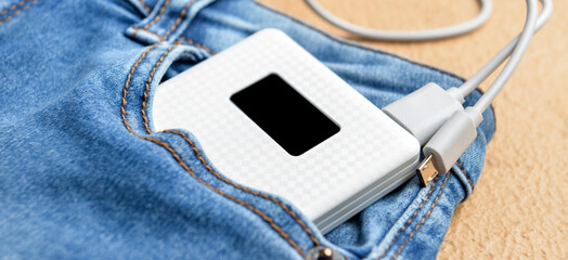 Modern power bank in pocket of jeans on beige background, closeup