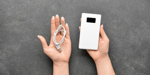 Woman holding modern power bank and USB cable on black background, top view - obrazy, fototapety, plakaty