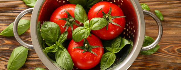 Colander with fresh basil and tomatoes on wooden background, top view