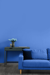 Comfortable sofa and table with vase of tulip flowers near blue wall in living room