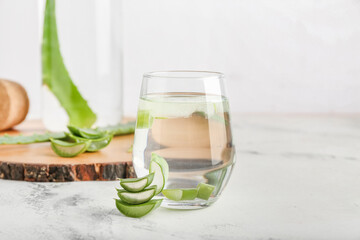 Glass of aloe juice and leaves on light background, closeup