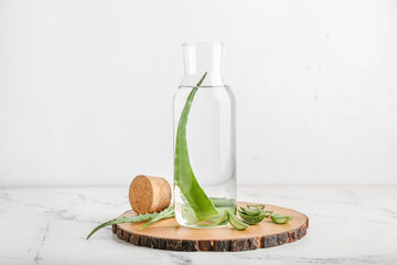 Board with glass bottle of aloe juice and leaves on white background