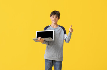 Teenage boy with laptop showing thumb-up on yellow background