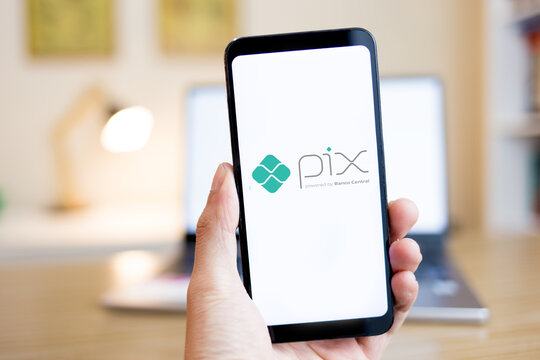 Hands holding a smartphone with the PIX logo on the screen with a house interior in the background. PIX is an instant money transfer and payment system in Brazil.