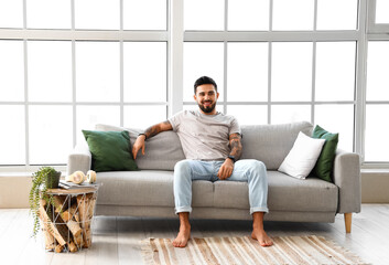 Handsome barefoot man sitting on sofa at home
