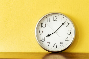 A clock on wooden table with yellow wall background, 8 o'clock 7 minutes