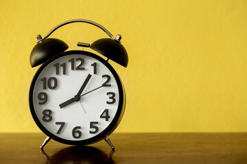 Black alarm clock on wooden board over yellow background, 8 o'clock 5 minutes