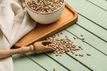Bowl, scoop with peeled sunflower seeds, board and napkin on green wooden background