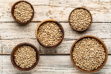 Bowls with peeled sunflower seeds on white wooden background
