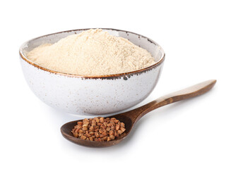 Bowl of flour and spoon with buckwheat grains on white background