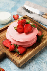 Wooden board with pink pancakes and strawberry on color background, closeup