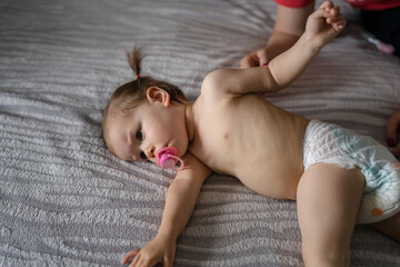 One female toddler in diapers lying down on bed in bedroom at home Childhood concept - obrazy, fototapety, plakaty