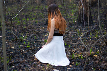 a girl with red hair in a black scorched forest. problems of ecology and environmental protection.