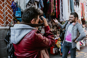Fototapeta na wymiar Pareja gay lgbt de hombres hispanos tomando retratos con cámara fotográfica en un mercado de artesanías en América Latina