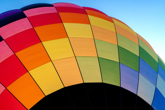 A colorful rainbow hot air balloon inflating against a blue sky