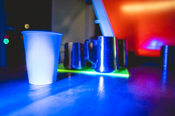 White paper cup with coffee, vintage coffee machine and coffee barista tools and jugs over a neon...