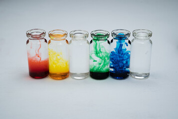 seis botellitas de vidrio con tintas diluidas multicolor y fondo blanco - obrazy, fototapety, plakaty