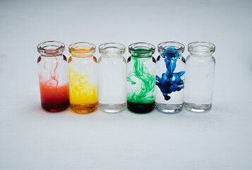 seis botellitas de vidrio con tintas diluidas multicolor y fondo blanco