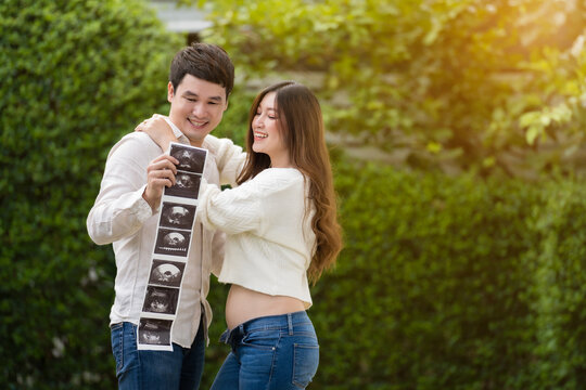 happy pregnant woman with husband watching ultrasound photo of baby. married couple.