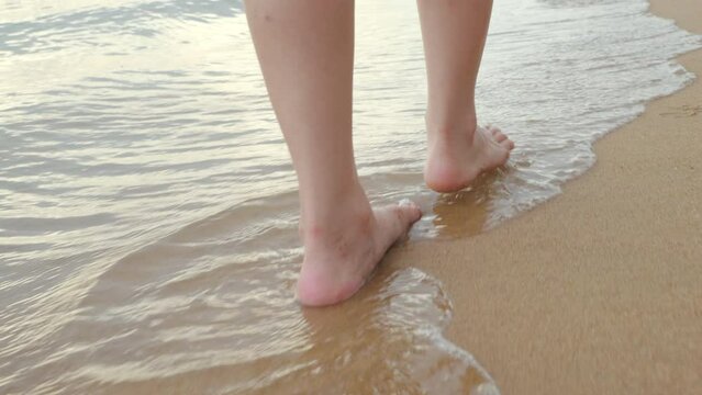 Back view, Close up foot of young beautiful woman walking into tropical on sand beach in water leaving footprints, Closeup detail of female feet walk  in the sand, Summer travel vacation concept