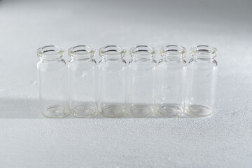 hilera de 6 botellas pequeñas de vidrio sobre fondo con textura claro, llenos de agua, simple y limpio.