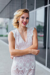 Beautiful blond bride in white wedding dress standing near mirror window outdoors.