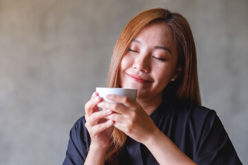 Portrait image of a beautiful young asian woman with closed eyes holding, smelling and drinking hot coffee