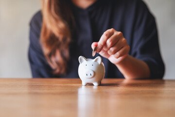 Closeup image of a woman putting coin into piggy bank for saving money concept - obrazy, fototapety, plakaty