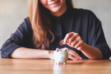 Closeup image of a young woman putting coin into piggy bank for saving money concept