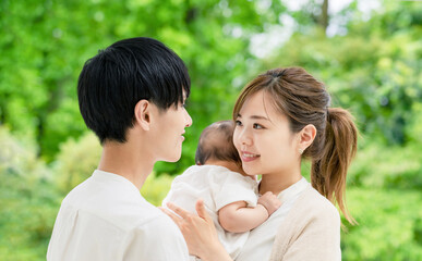 Fototapeta premium 新緑を背景に赤ちゃんを抱っこするカップル 子育てイメージ
