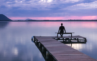 Man sitting on a wooden pier bench watching the sunrise at Lagoa da Conceicao in Florianopolis - Brazil. - Powered by Adobe