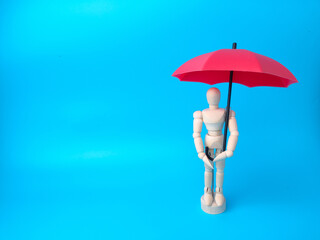 Wooden mannequin holding red umbrella on a blue background with copy space. Insurance and protection concept.