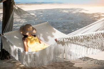 Happy Woman Traveler is relaxing in a hammock on the paradise beach. Female tourist in yellow dress...