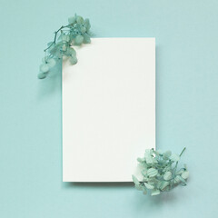 Blank white memo paper with dry flowers on blue background. top view, copy space