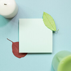 Blank memo paper with candle, leaf on blue background. top view, copy space