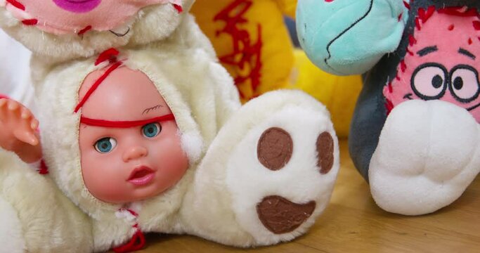 Face of baby doll put into torn belly of white teddy bear. Scary monsters sewn from different toys put in row on wooden floor close view