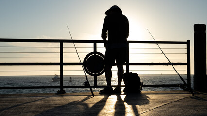 silhouette of a fisherman working on a pole on a harbor
